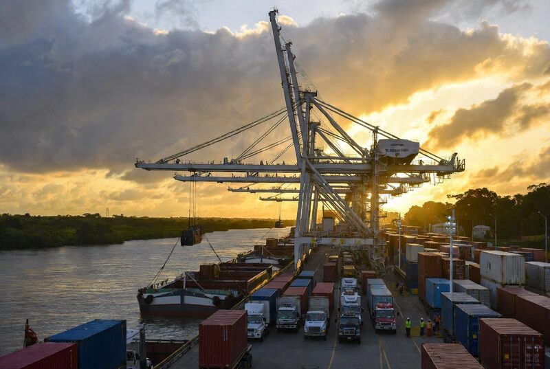 Grúa cargando contenedores sobre barcazas en un puerto fluvial
